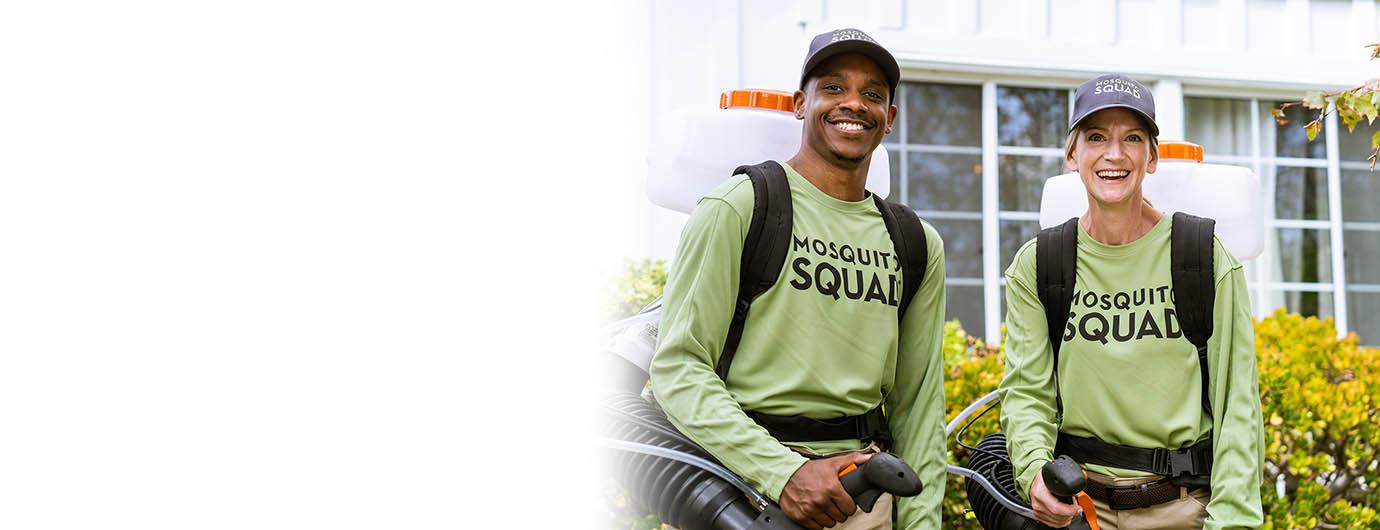Two smiling Mosquito Squad technicians in green uniforms with backpack sprayers, ready for service in a residential area.