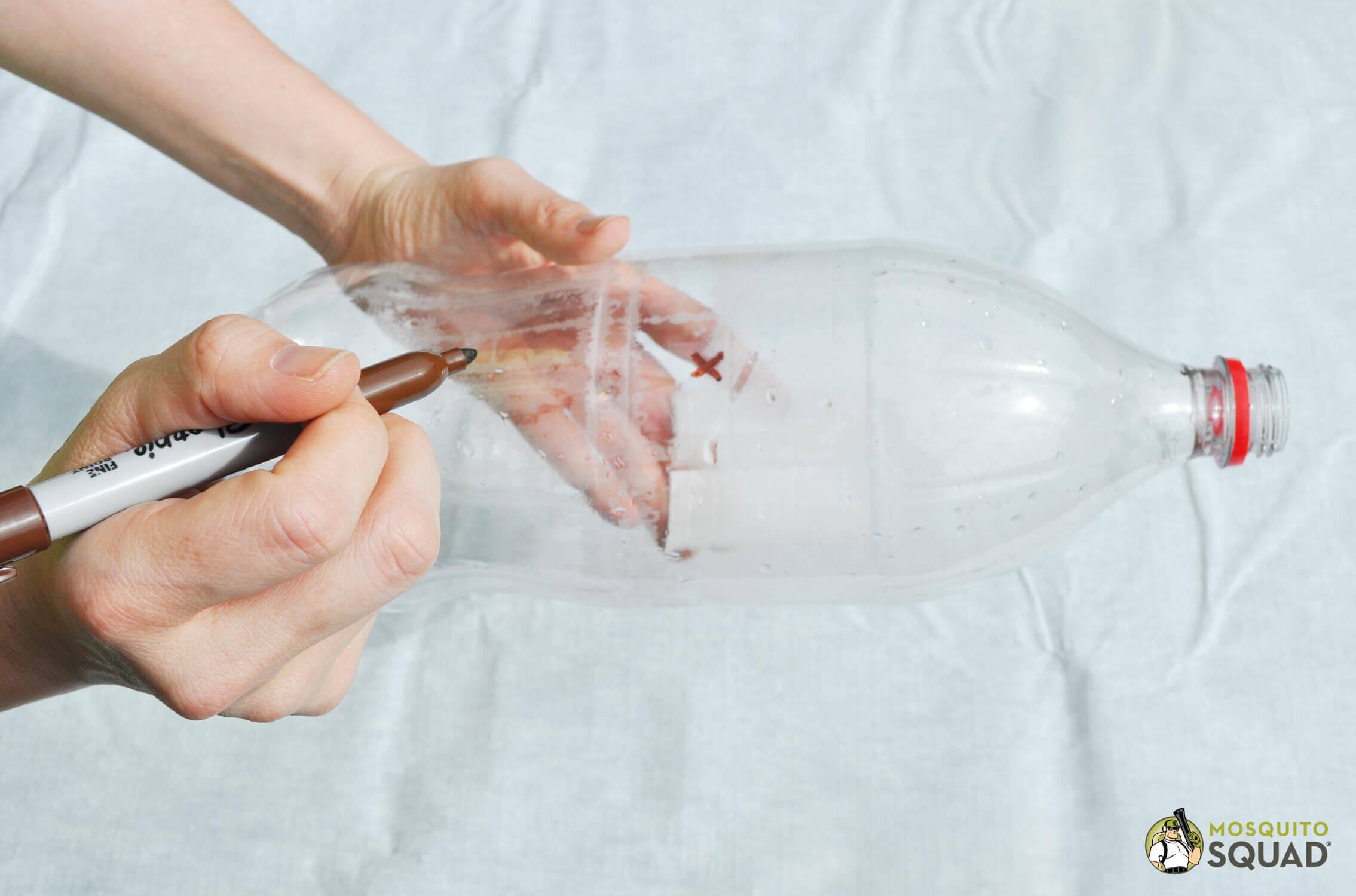 hand marking an x about halfway down a plastic bottle