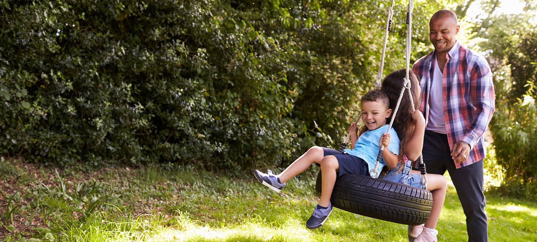 man pushing kids on tire swing