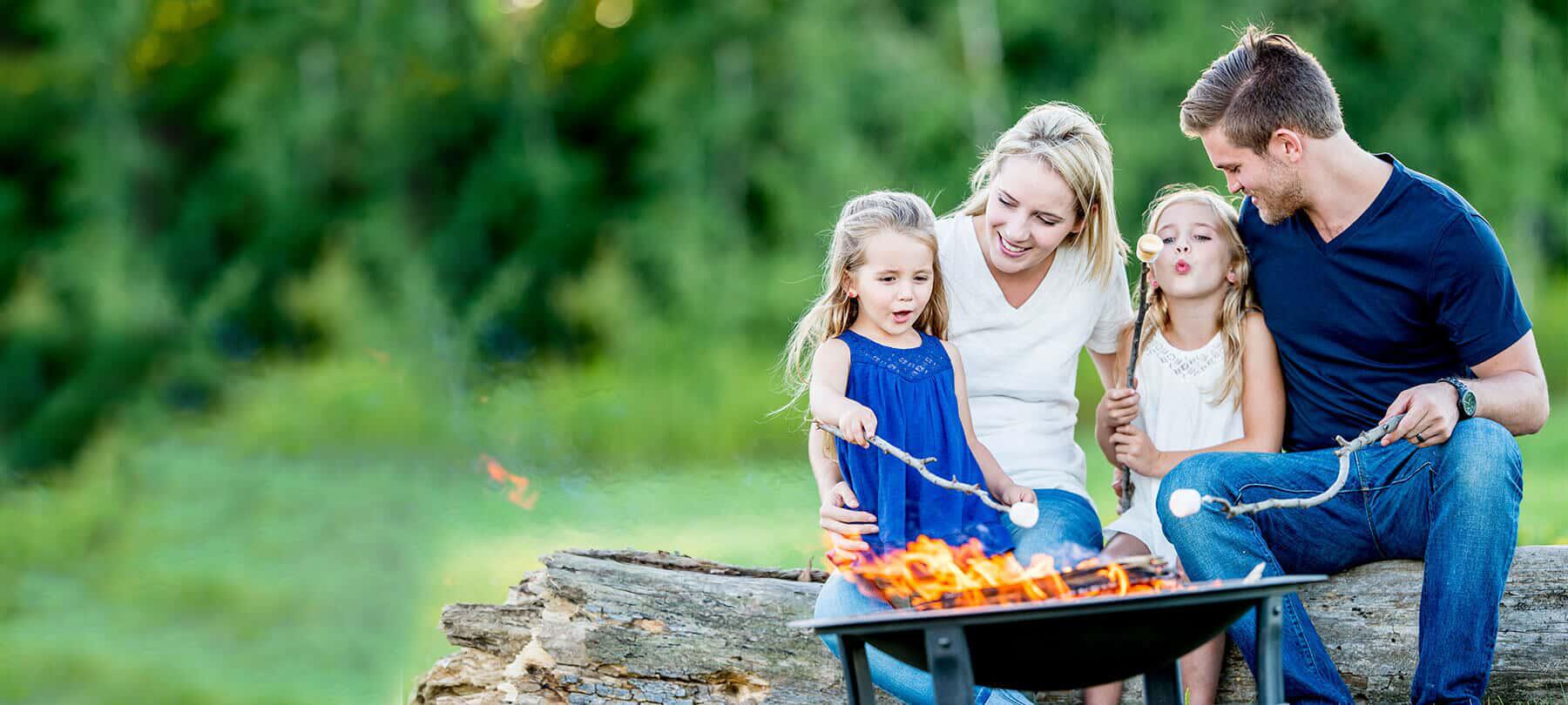 family sitting on log near fire pit