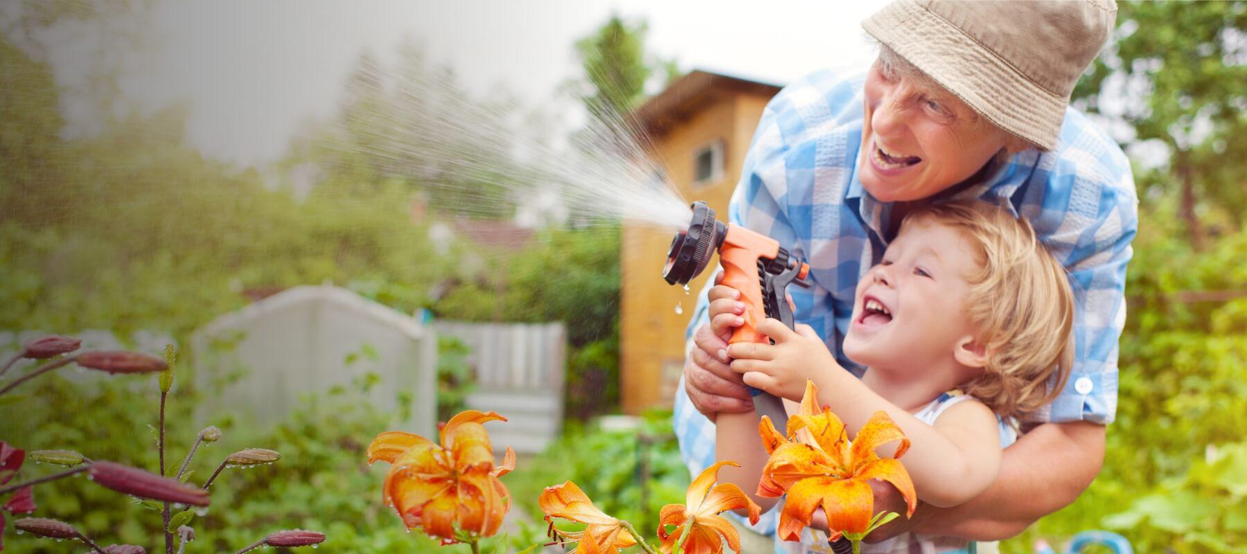 man spraying hose with child