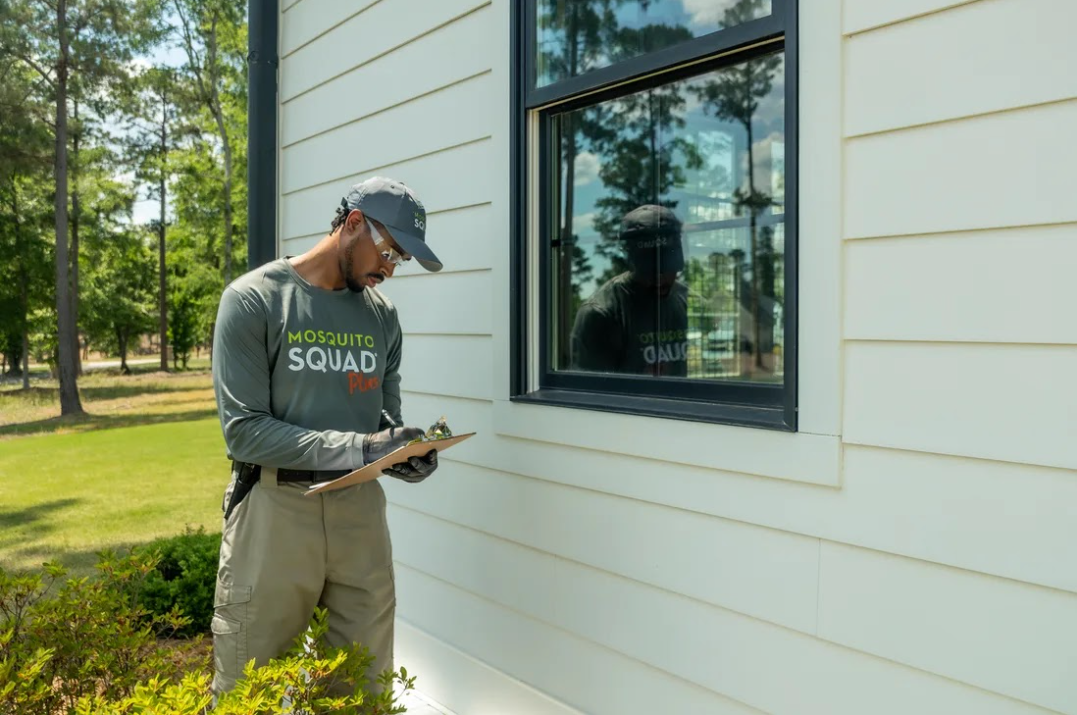 Technician with a clipboard inspecting the outside of a home for rodent entry points